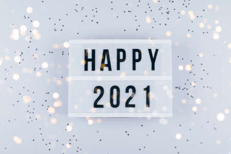 Happy New Year 2021 celebration. Light box with text Happy 2021 and sparkles on gray background.