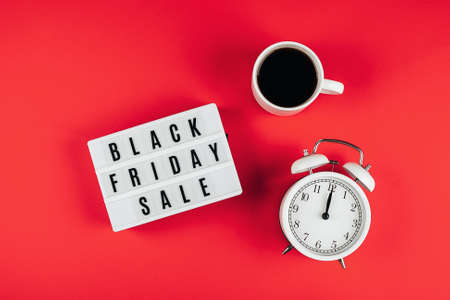 Black friday sale word on lightbox, cup of coffee, alarm on red background table. Flat lay, top viewの写真素材