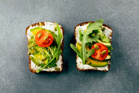 Healthy vegan snack. Avocado toasts with cottage cheese, arugula, tomato on wooden board, cup of...