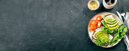 Avocado toasts with cottage cheese, arugula, cup of coffee on dark table. Healthy breakfast, snack. Top view, copy spaceの写真素材