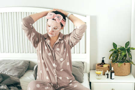 Mature women in sheet mask in pajama spending cozy morning during isolation period, reading book.の写真素材