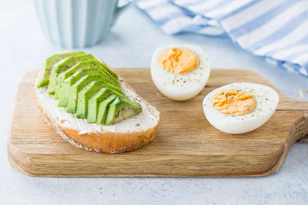 White desktop table with laptop, fresh toast with avocado, mug of coffee and Havortia. Woman...