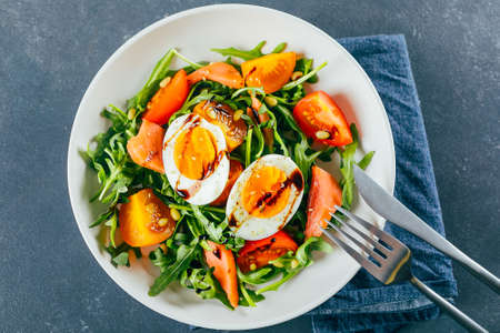 Healthy vegan salad of fresh tomato, arugula, salmon, egg and sesame on plate. Diet menu. Top view