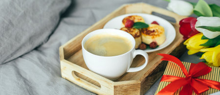 Breakfast in bed. Mother's day, birthday, 8 march, valentines day concept. Healthy branch - coffee, cottage cheese, pancakes, gift box and fresh tulips. Banner for design, websiteの写真素材