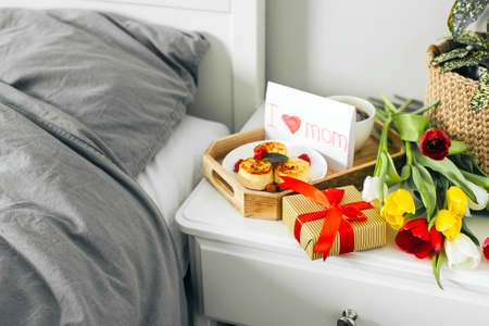 Delicious breakfast for holiday morning. Mother's day, birthday, 8 march, valentines day concept. Package gift box, colorful tulips, hot coffee, cottage cheese pancakes.の写真素材