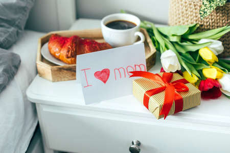 Children card on Mother's day Holiday. Tasty breakfast, cup of coffee, gift box and spring flowers tulips. Valentine's day, march 8 conceptの写真素材