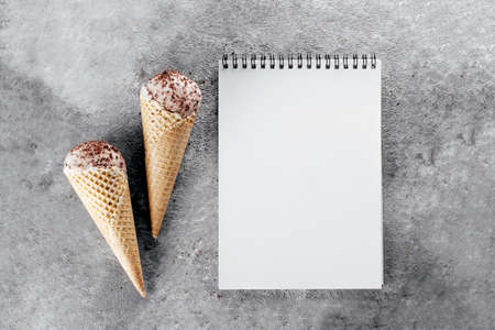 Banner Image. Chocolate ice cream in waffle cones and text in small wooden letters Hello Summer on...