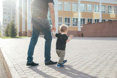 Father and Son walking together. Baby taking first steps with father help. Authentic moment, summer...