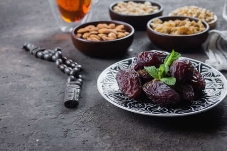 Ramadan kareem. Fresh Dates on plate and rosery beads on light concrete background. Top view.
