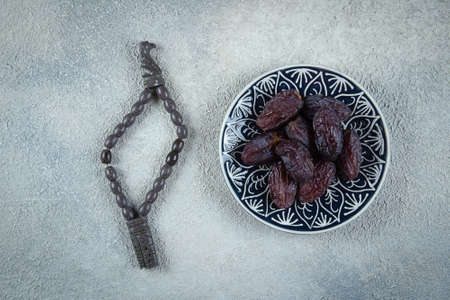Ramadan kareem. Fresh Dates on plate and rosery beads on light concrete background. Top view.の写真素材
