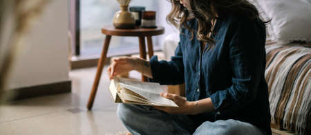 Beautiful middle age asian woman sitting in bed at home and reading book. Concept of home relax, home lifestyleの写真素材