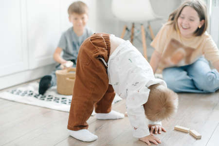 Children play on the floor of the children's room. Little brother amuses his brother and sister stands on his head at home. family lifestyle conceptの写真素材