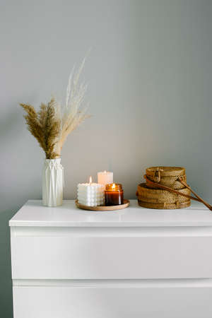 Home interior decor in beige neutral colors. White dresser with dried flowers in vase, rattan bags and candle. Still life, hygge concept. selective focusの写真素材