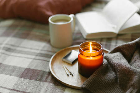 Burning candle with wooden wich in amber glass gar, open book and cup of coffee or tea. Cozy lifestyle, hygge conceptの写真素材