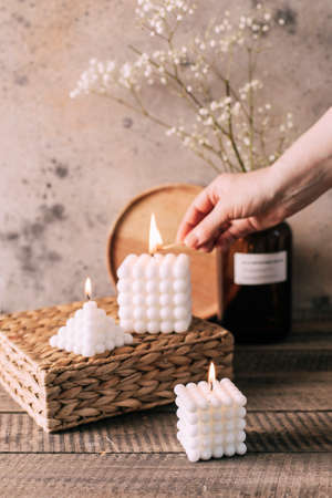 Female hand lights candles. Three white babble candles on straw stand on wooden background.の素材 [FY310190131863]