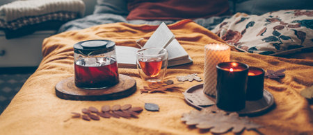 Cozy bed with cup of tea, candles and open book. Concept of autumn cozy home interior, wellbeing, relaxation on weekendの写真素材