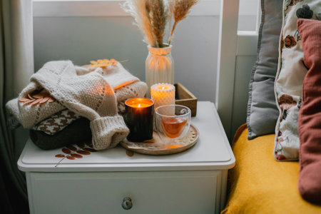 Cozy bed with cup of tea, candles and open book. Concept of autumn cozy home interior, wellbeing, relaxation on weekendの写真素材