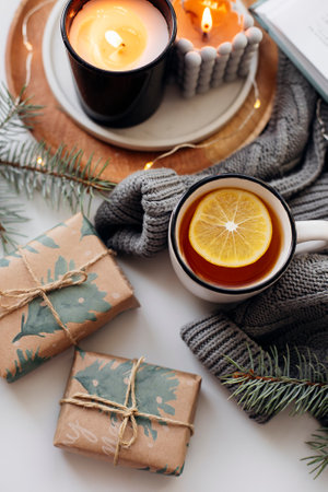 Winter home cozy concept. Mug with lemon tea, open book, warm sweater, candles and fir tree. Wellbeing, relaxing concept.の写真素材