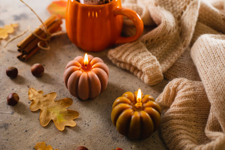 Burning candles shape of pumpking, mug with aiutumn drink, leaves and cinnamon. Autumn mood, hygge atmosphere.の写真素材