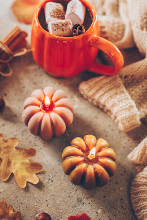 Burning candles shape of pumpking, mug with aiutumn drink, leaves and cinnamon.の写真素材