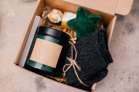 Christmas box with presents - candle in dark jar, chocolate candies, cozy gray socks and festive decoration. Personalized craft box for winter holidays.の写真素材