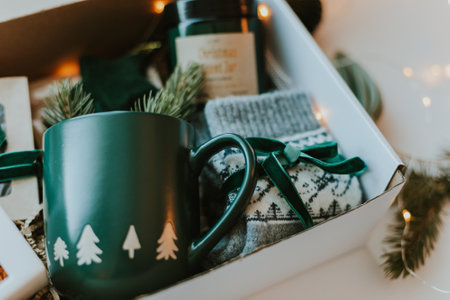 Close-up of Christmas gift box. Cozy mug for coffee, warm gray socks, aroma candle in jar