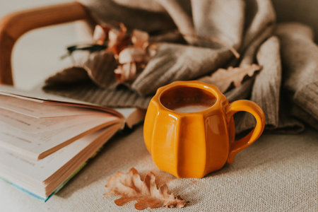 Warm autumn ambiance featuring a pumpkin-shaped mug with coffee surrounded by seasonal decorations like pumpkins, leaves, and a candle on a rustic wooden surface.の写真素材