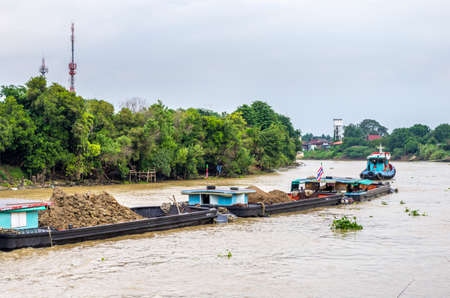 Ayutthaya, Thailand - July 07, 2013   Tug boat towing barges filled with ore on the Chao Phraya river in Ayutthaya, Thailand のeditorial素材