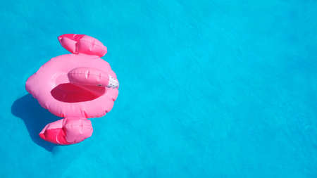 Flat lay inflatable pink flamingo swims in clear blue azure pool water. Summer concept of...