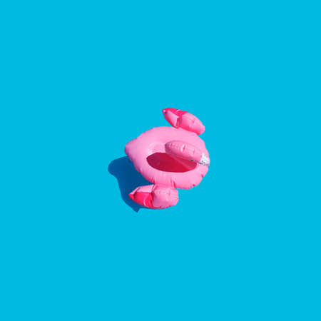 Flat lay of isolated in the center of an inflatable toy pink flamingo with a shadow on a blue azure...