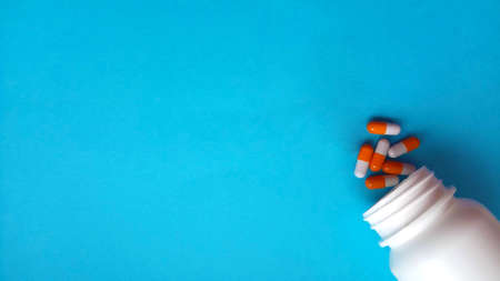 Red-white pharmaceutical medicine pills, tablets and capsules spread out of white plastic drug...
