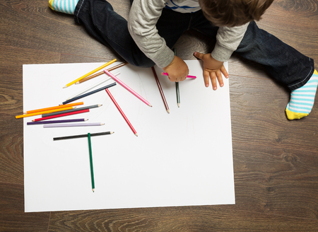 Toddler boy drawing on the white sheet of paper sitting on the floorの写真素材