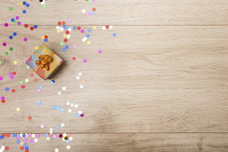 Gift box and colorful confetti on a wooden background