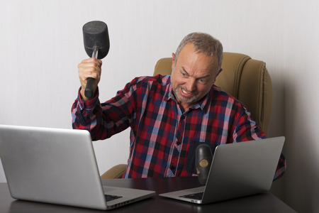 Angry man crashing laptop with a hammerの写真素材