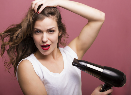 Pretty woman styling her hair with a hairdryerの写真素材