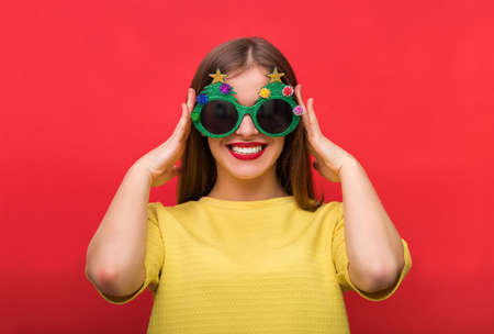 Woman with Christmas party glasses standing against a red background