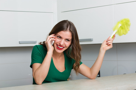Woman with duster brush cleaning up her kitchen