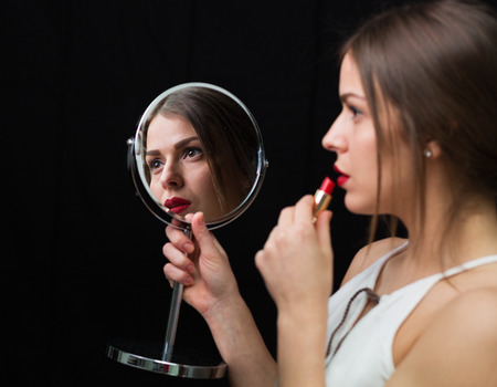 Beautiful woman applying red lipstick and holding mirrorの写真素材