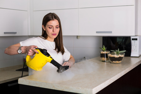 Young beautiful woman cleaning kitchen with steam cleanerの写真素材