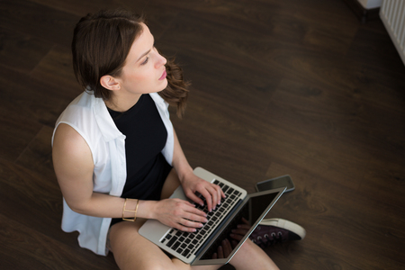 Young stylish woman sitting on the floor and working at the laptopの写真素材