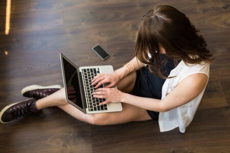 Young stylish woman sitting on the floor and working at the laptopの写真素材