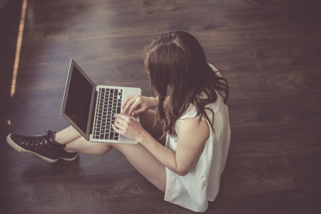 Young stylish woman sitting on the floor and working at the laptopの写真素材