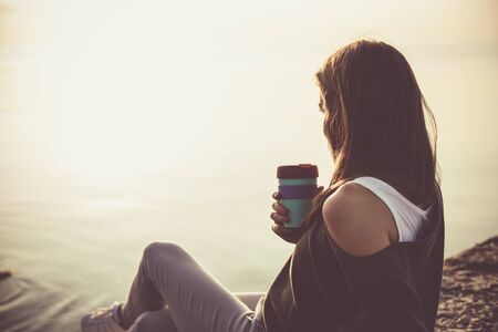 Young woman drinking coffee on the beach in the morningの写真素材