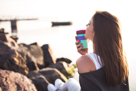 Young woman drinking coffee on the beach in the morning