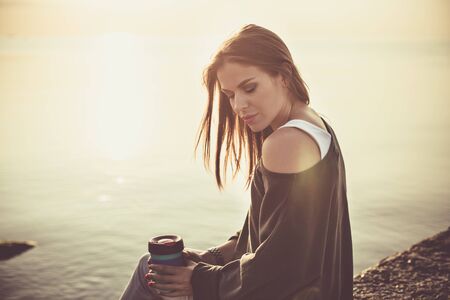 Young woman drinking coffee on the beach in the morning