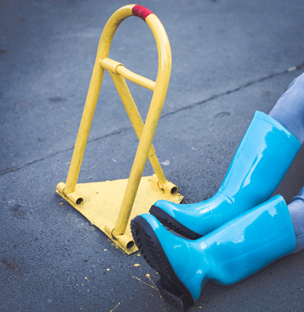 Woman in blue rainboots sitting near a yellow parking stop