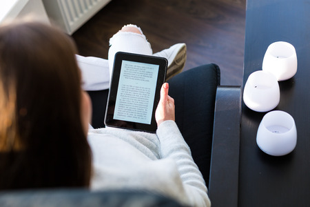 Young woman sitting by the window with an e-book