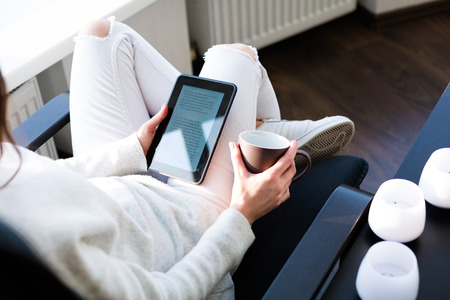 Young woman sitting by the window with an e-bookの写真素材