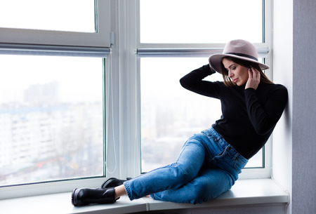 Beautiful boho woman in wool hat sitting by the windowの写真素材