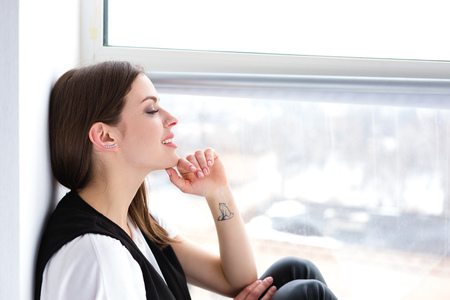 Beautiful happy woman sitting and daydreaming by the windowの写真素材